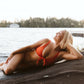Girl laying on a rock by the lake wearing a burnt orange bikini.